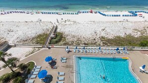 A beachside pool area with lounge chairs and umbrellas, a clear view of the ocean, and a sandy beach in the background.