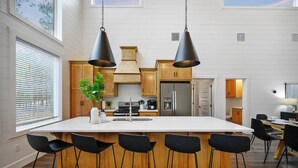 A modern kitchen with a large island, wooden bar stools, and pendant lighting. - NEW Spectacular Modern Retreat -The Fika House-Lux (Broken Bow)
