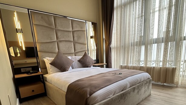 Une chambre à coucher moderne avec un grand lit, une table de chevet, un miroir et une fenêtre agrémentée de rideaux légers.