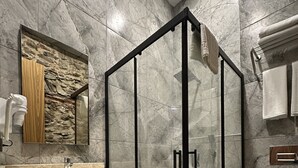 Une salle de bain moderne avec une douche à parois de verre, un meuble-lavabo en bois avec un miroir et un mur recouvert de carreaux de marbre.