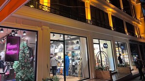Un immeuble à plusieurs étages doté de balcons et de devantures de magasins illuminés, parmi lesquels une boutique et un magasin où est installé un sapin de Noël.