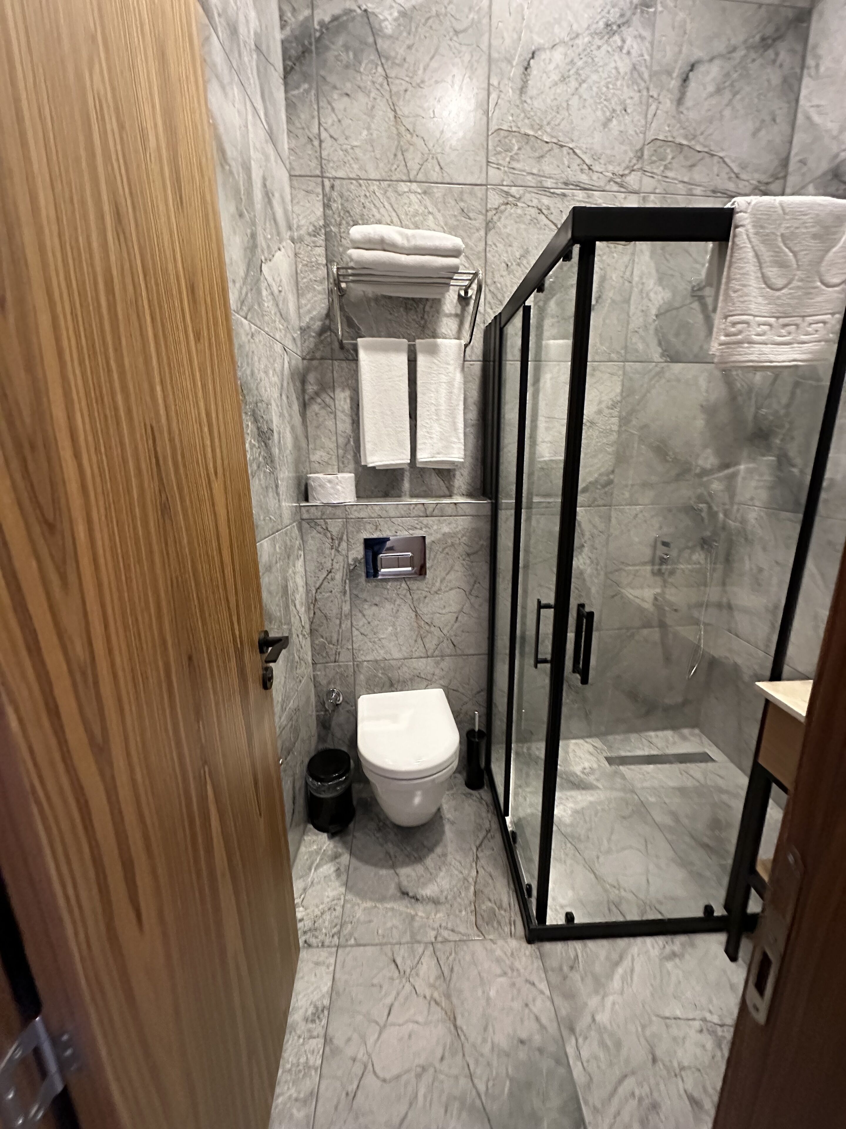 Une petite salle de bain comprenant des toilettes, une douche en verre et un sol carrelé en marbre.