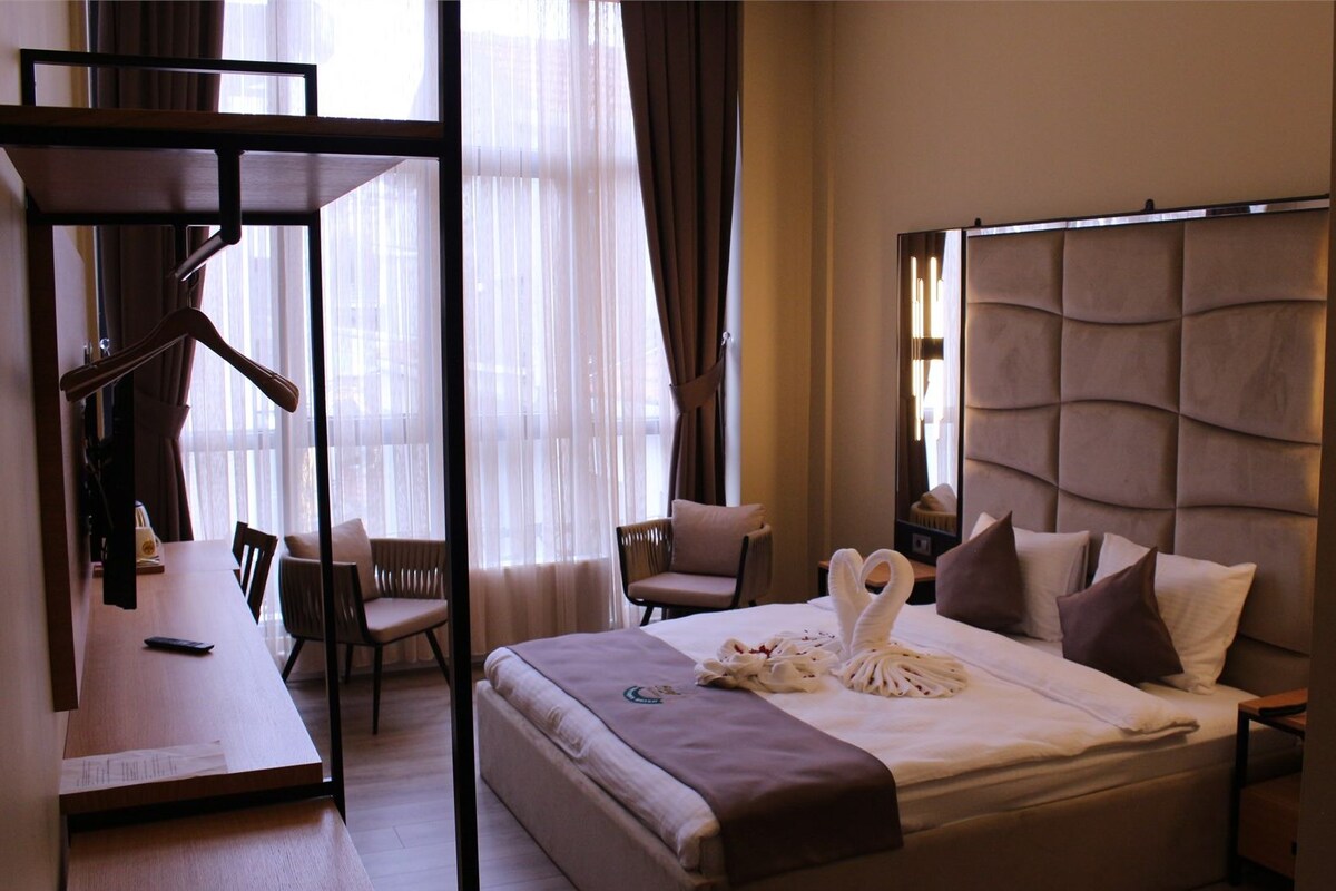 Una habitación de hotel con una cama, dos sillas, un escritorio y un ventanal con cortinas.
