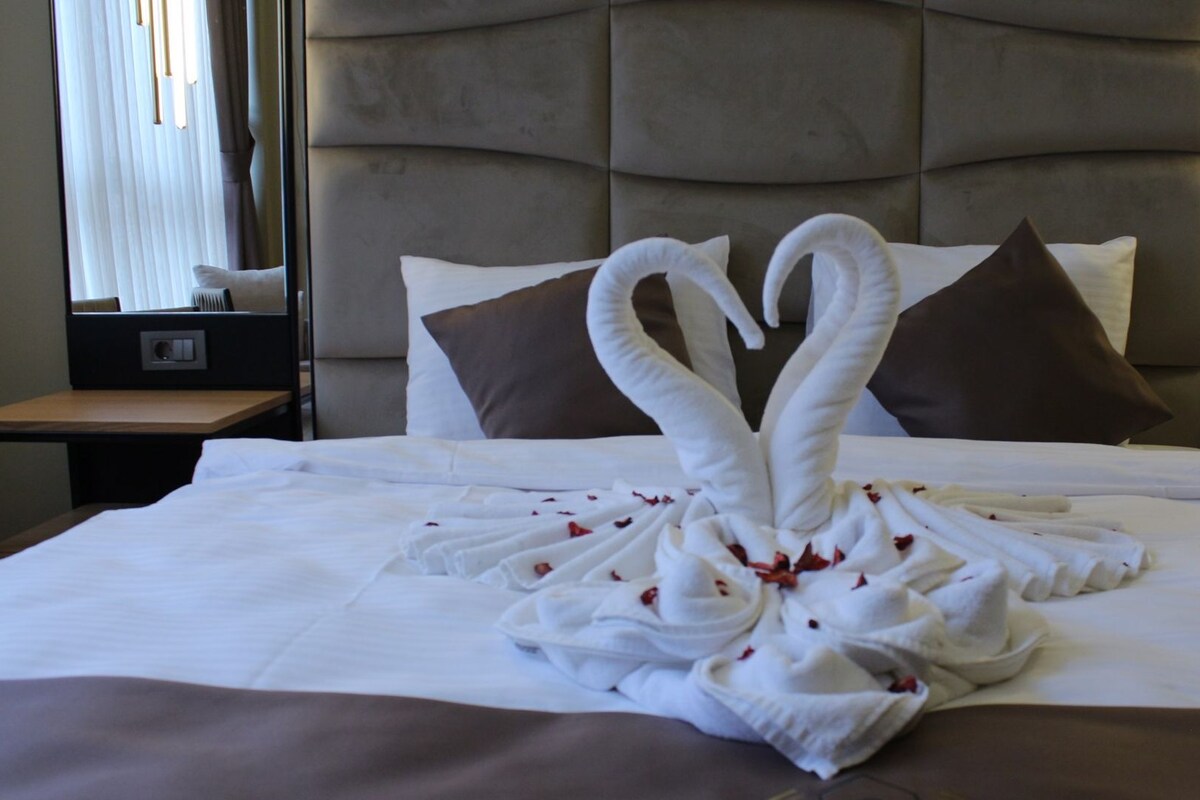 A hotel room with a large bed, a tufted headboard, two nightstands, and a mirror.