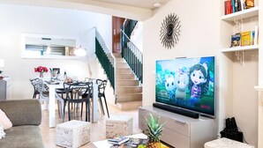 Ein modernes Wohnzimmer mit Flachbildfernseher, Essbereich und einer Treppe.