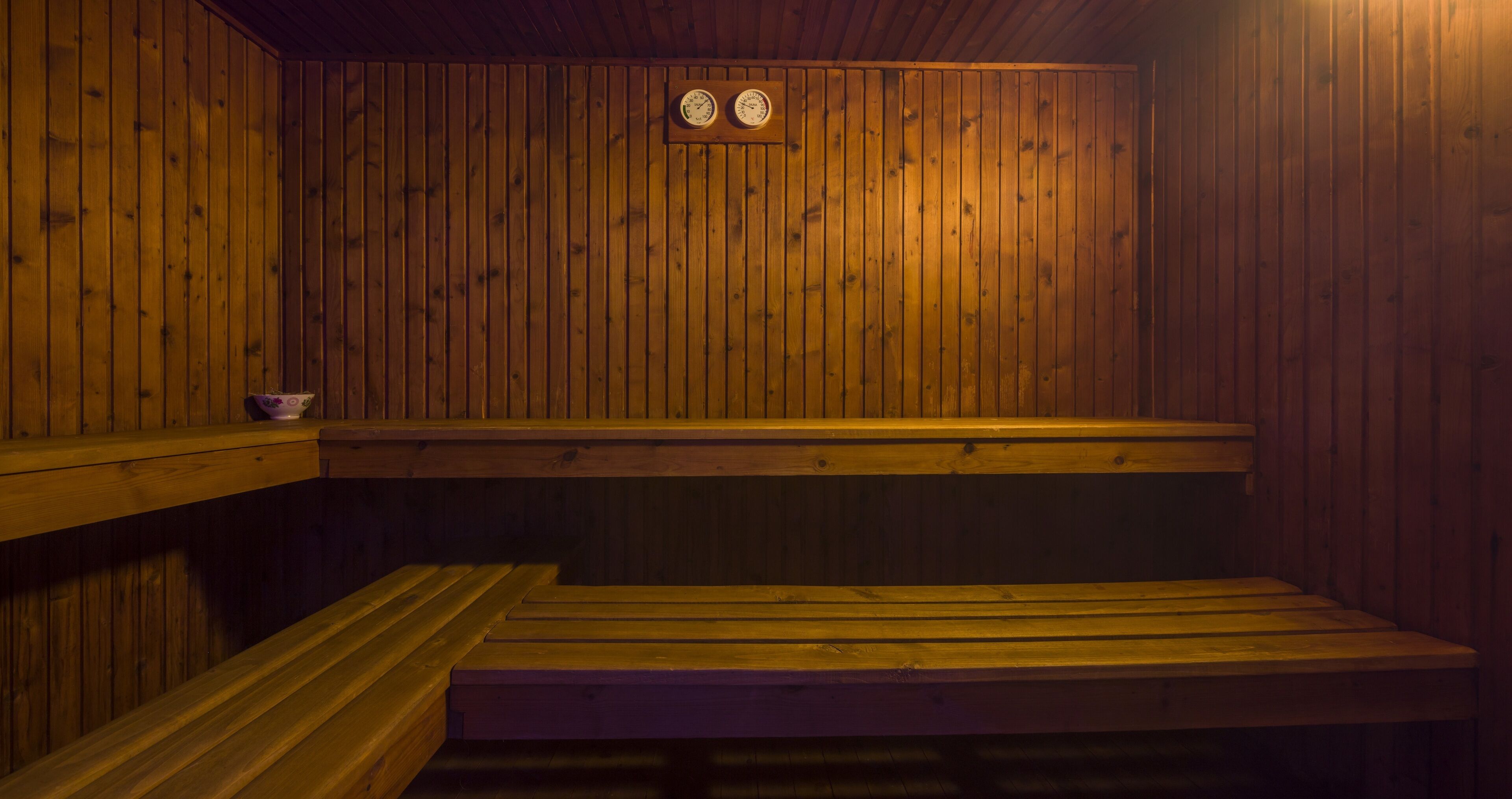 Una sauna con bancos de madera y un pequeño estante con un cuenco.