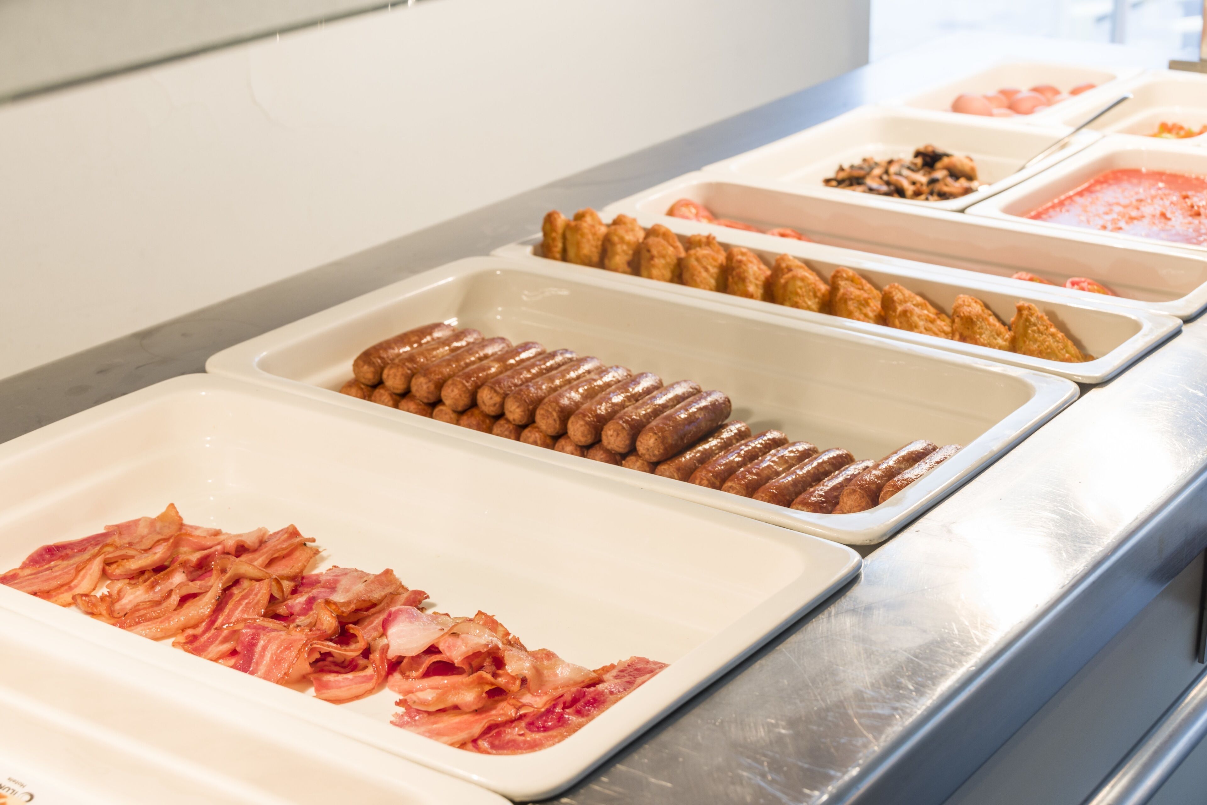 A buffet with various food options including bacon, sausages, and other prepared dishes.