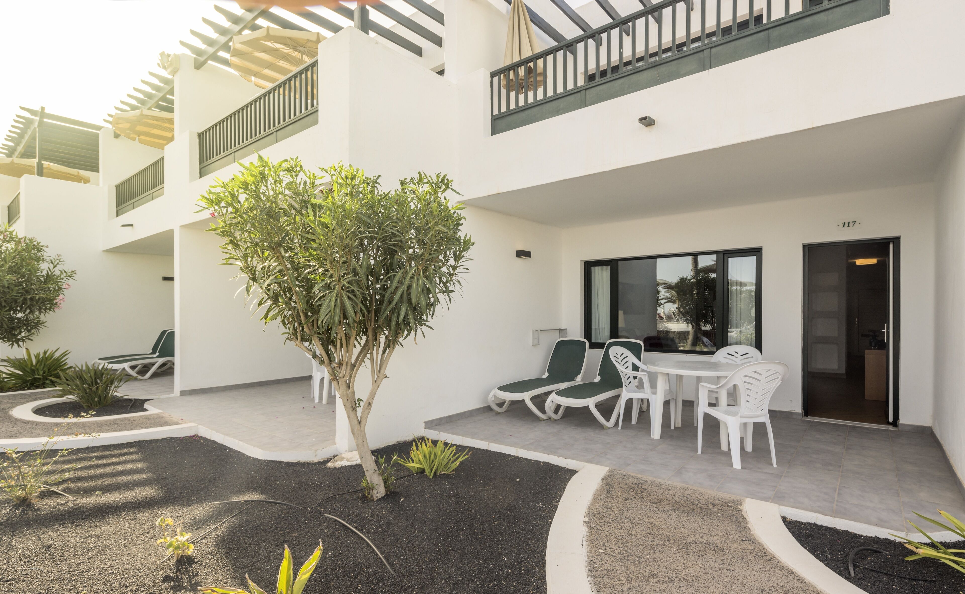 Une cour avec un petit arbre, des sièges extérieurs et un bâtiment doté d’un balcon.