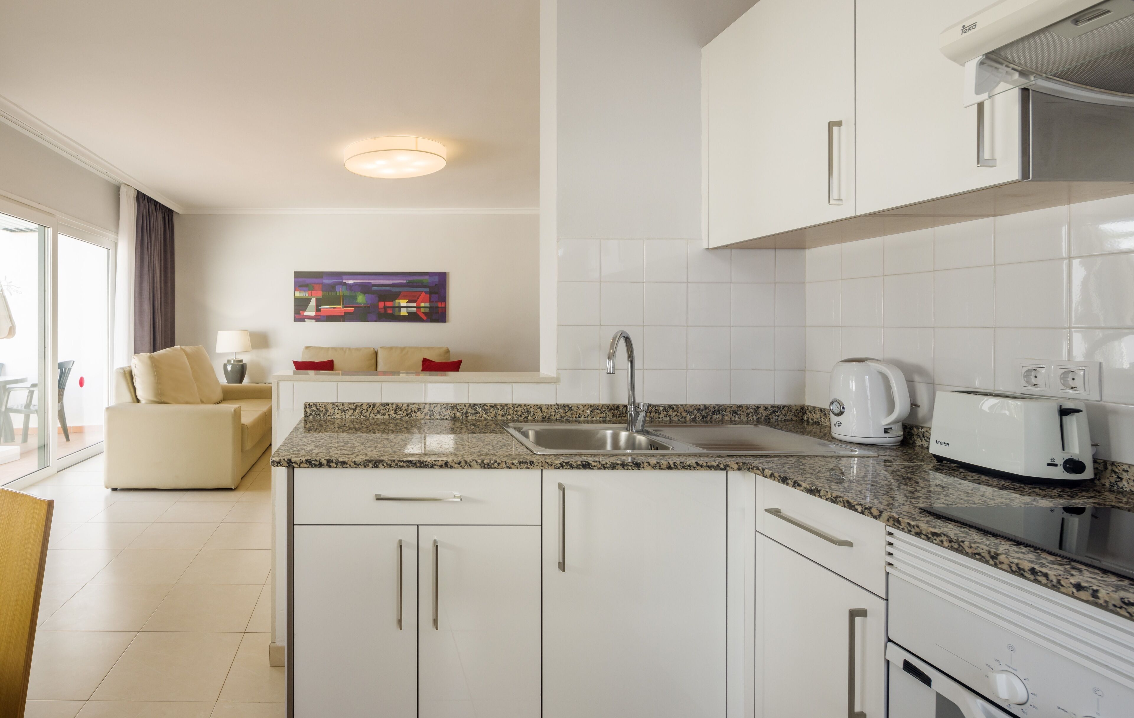 A modern kitchen with white cabinets, granite countertops, a built-in oven, and a coffee maker.
