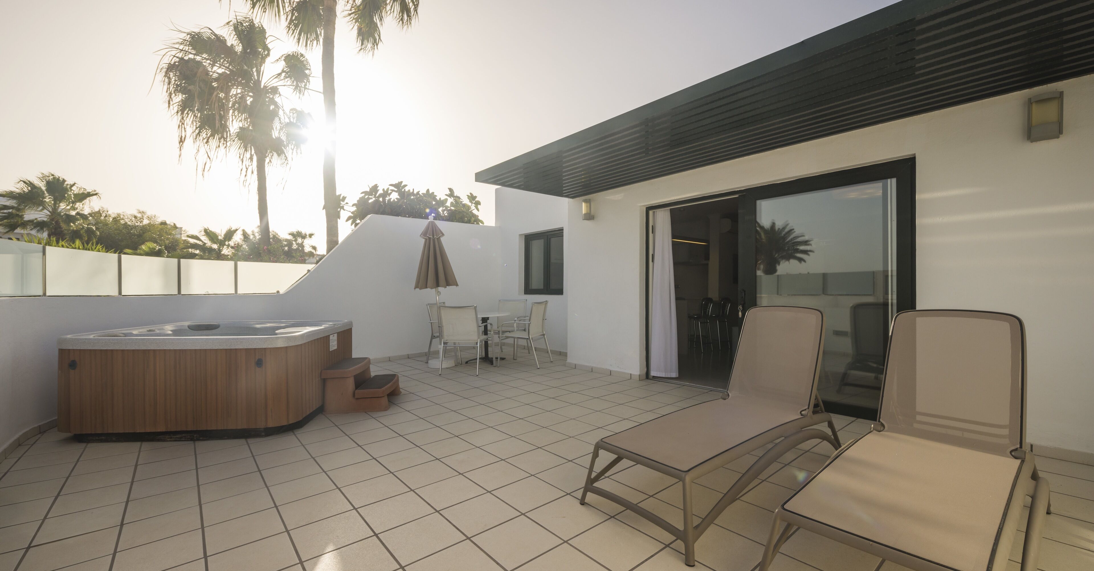 A modern outdoor patio with a hot tub, lounge chairs, and a dining area.