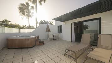 A modern outdoor patio with a hot tub, lounge chairs, and a dining area.