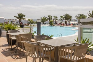 Zona de piscina con sillones y mesas, con vista al agua.