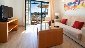 Una sala de estar moderna con sofá, mesa de centro, televisor y un balcón con mobiliario exterior.