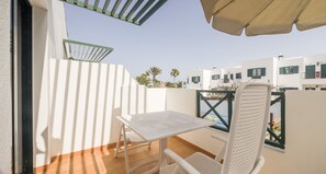 A balcony with a white table and chairs, a green metal railing, and a view of white buildings with green shutters. - Aparthotel ILUNION Costa Sal Lanzarote (Tías)