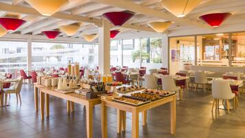 A spacious dining area with multiple tables and chairs, a variety of food and drink options, and large windows offering a view of the outside.
