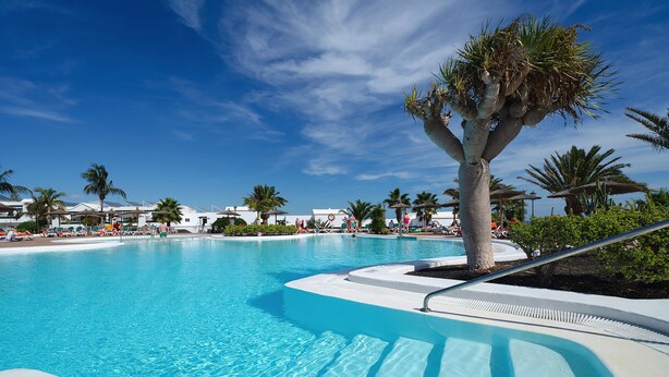 Una gran piscina cristalina rodeada de palmeras y sombrillas.