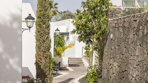 Un camino que lleva a un edificio con muro de piedra y fachada blanca.