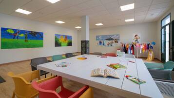 Un aula con una larga mesa, sillas coloridas, carteles educativos y una exposición de ropa infantil.