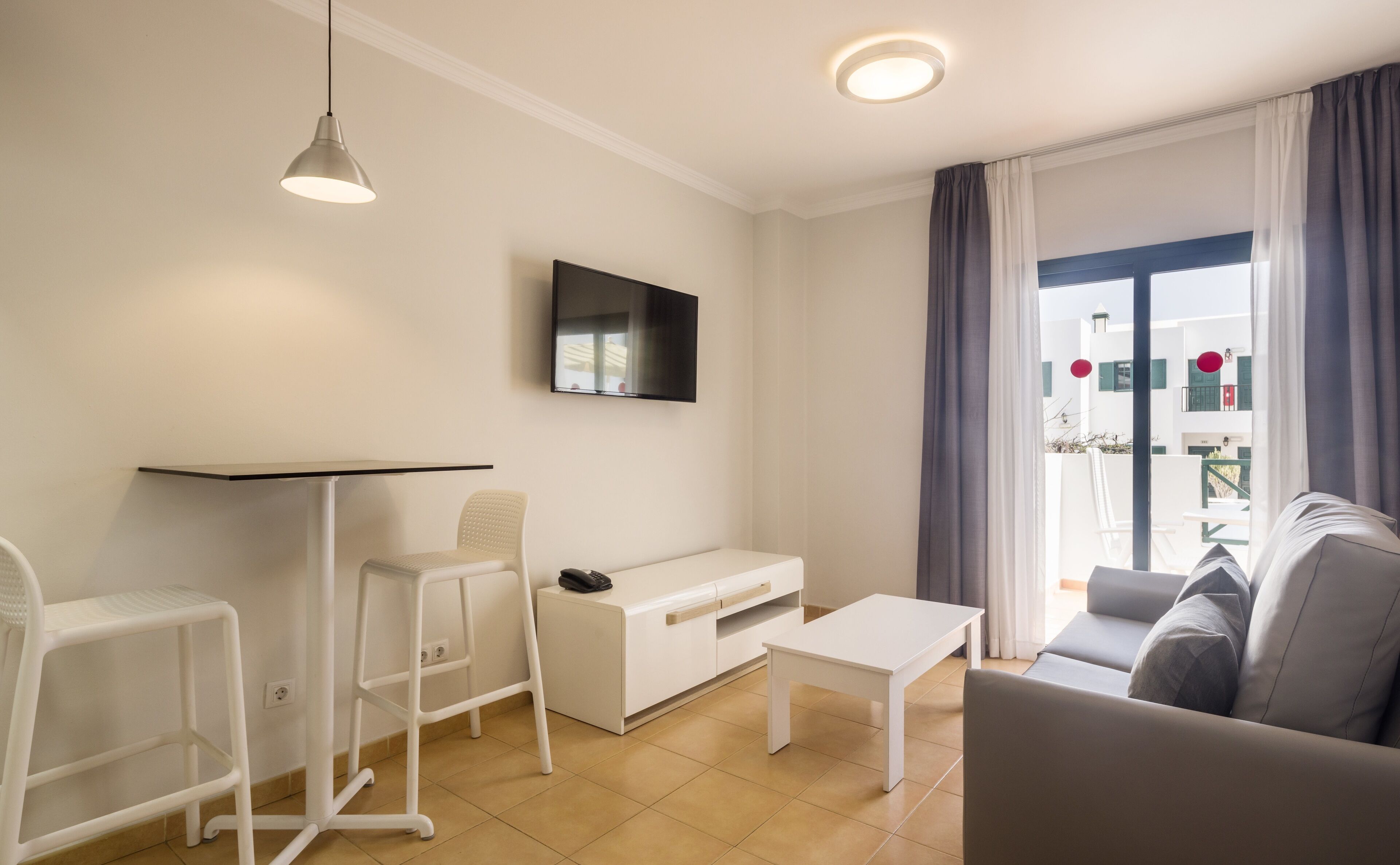 A modern living room with a white sofa, a white coffee table, a white TV stand, and a white desk with a chair.
