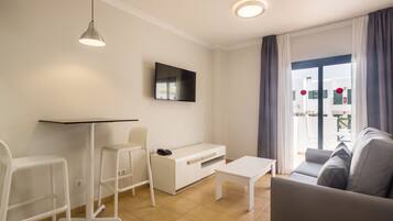 A modern living room with a white sofa, a white coffee table, a white TV stand, and a white desk with a chair.