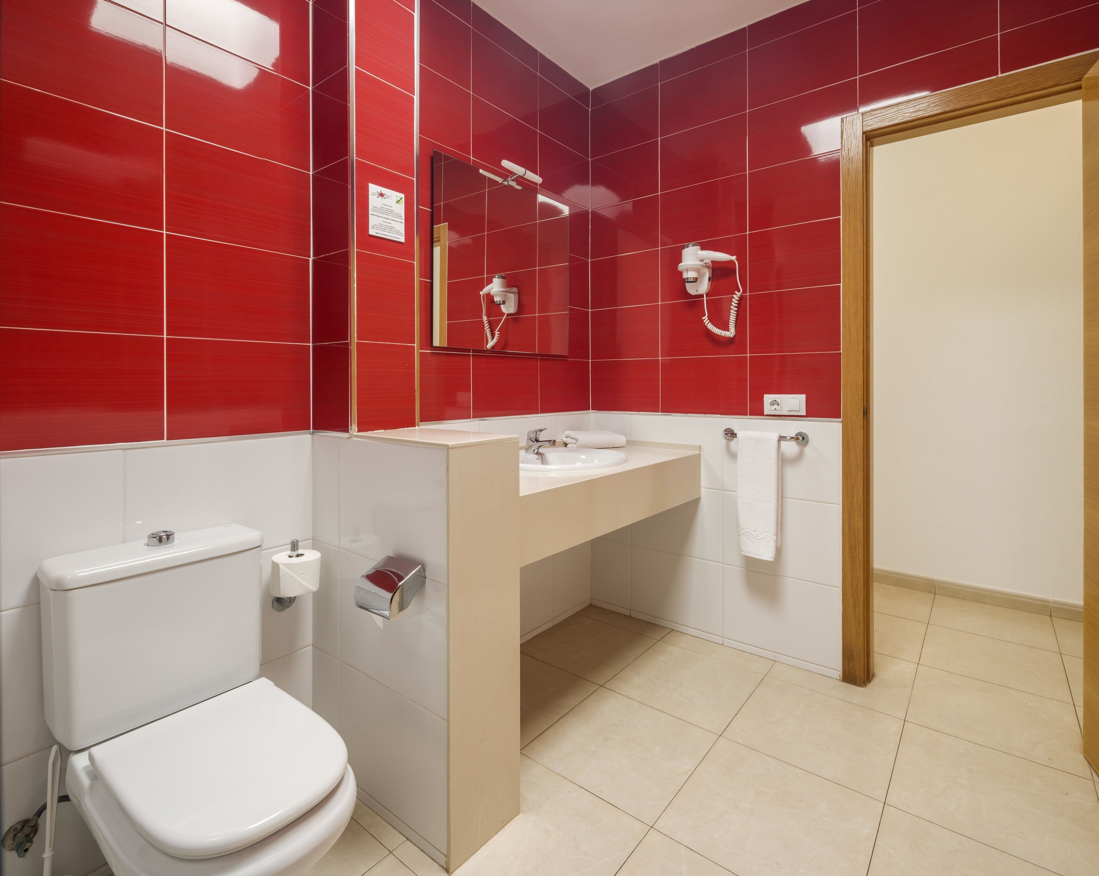 Un baño con azulejos rojos, un inodoro blanco, un lavabo y un perchero para toallas.