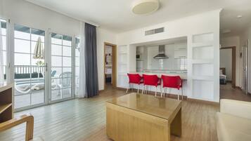 A modern living room with a glass coffee table, red chairs, a TV, and a sliding glass door leading to an outdoor area with a table and chairs.