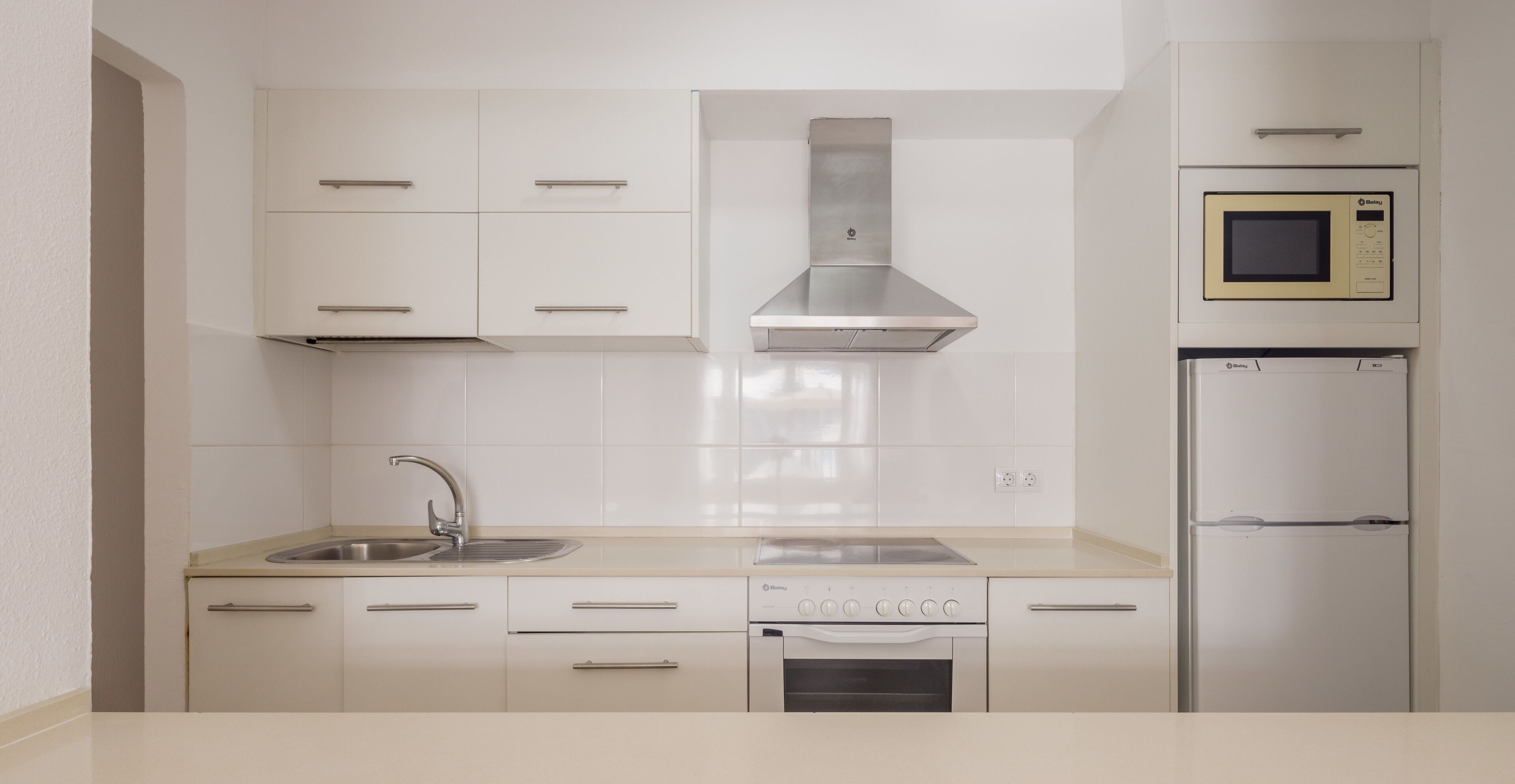 A modern kitchen with white cabinets, a stainless steel range hood, a microwave, and a refrigerator.