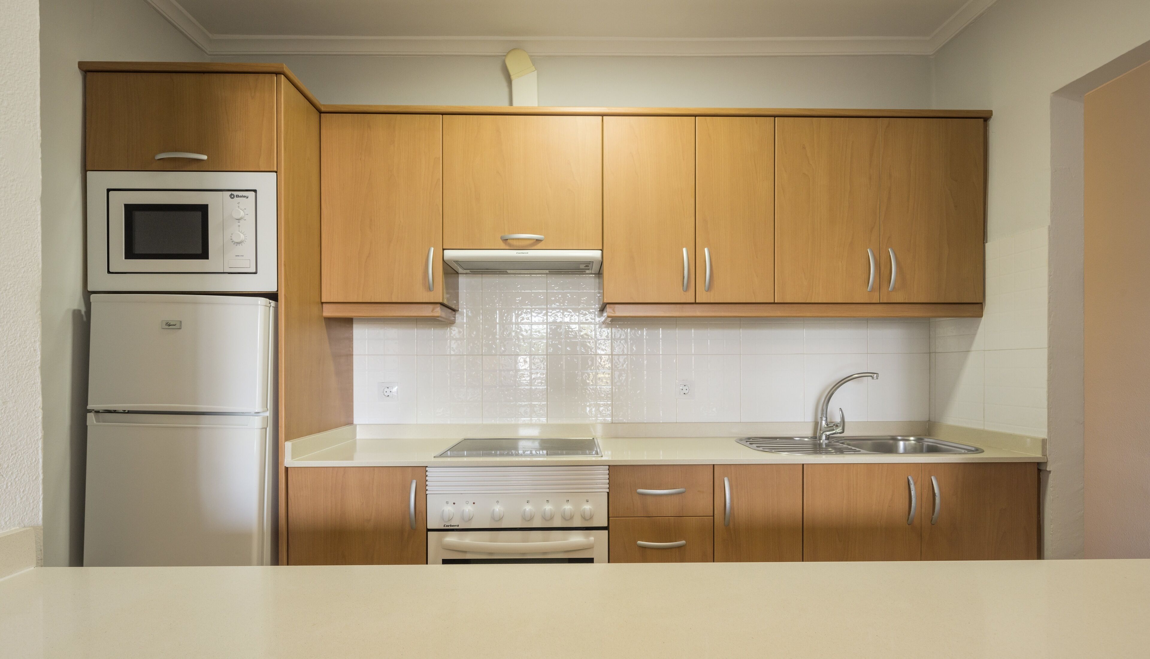 Una cocina compacta con armarios de madera, un microondas integrado, una estufa y un lavamanos.