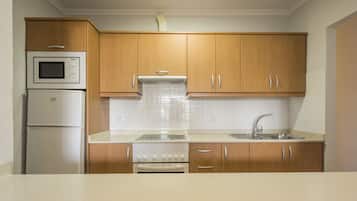 Una cocina compacta con armarios de madera, un microondas integrado, una estufa y un lavamanos.