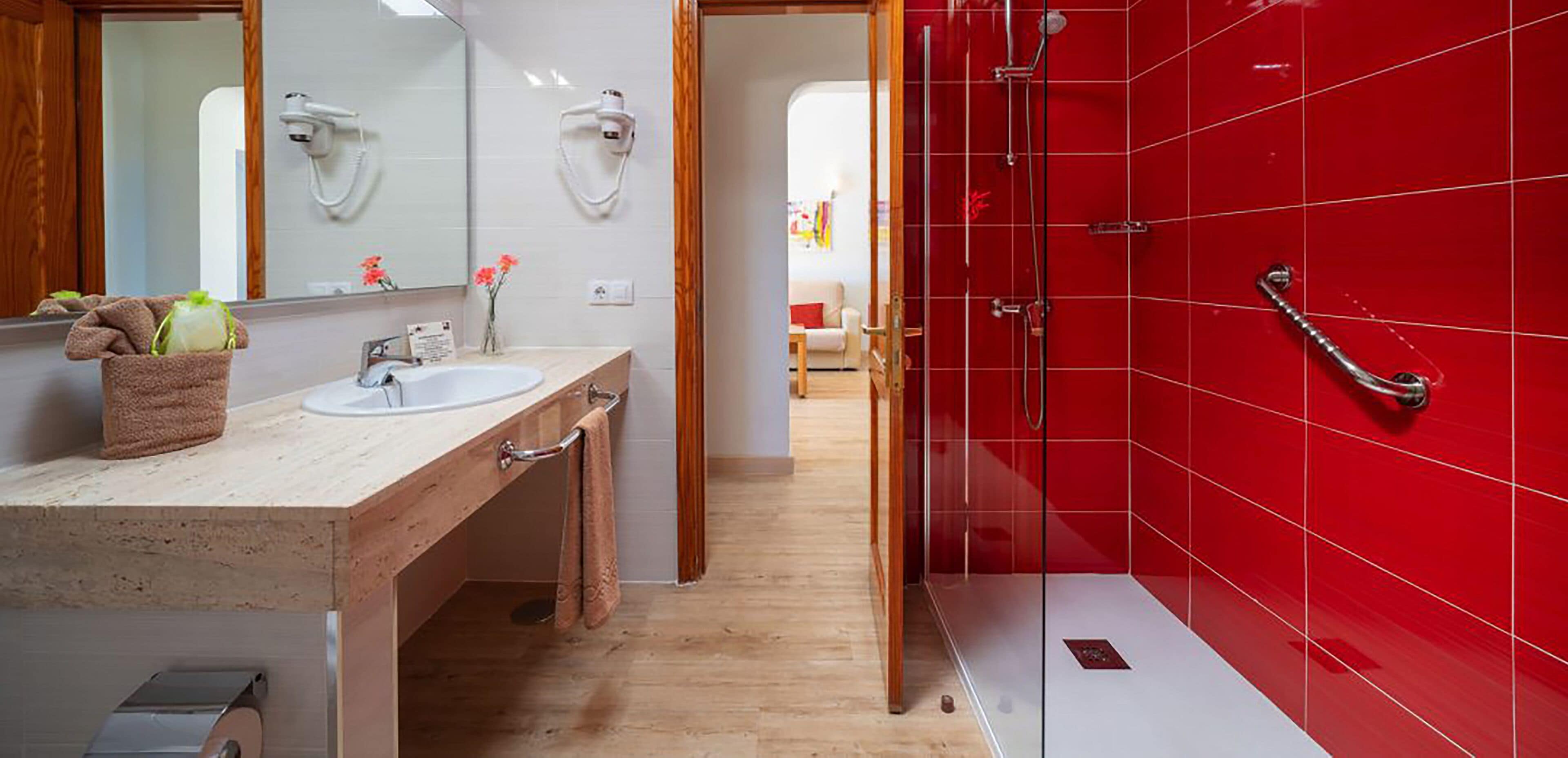 A modern bathroom with a wooden vanity, a white sink, and a red shower enclosure.