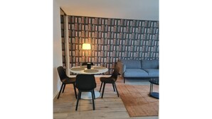 Een moderne woonkamer met een ronde eettafel, twee zwarte stoelen, een grijze bank en een boekenplank vol boeken.