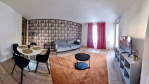 Een woonkamer met een ronde tafel, een bank, een boekenkast en een televisie.