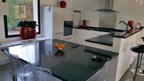 Une cuisine moderne avec une table à manger en verre, des meubles blancs et un plan de travail noir.