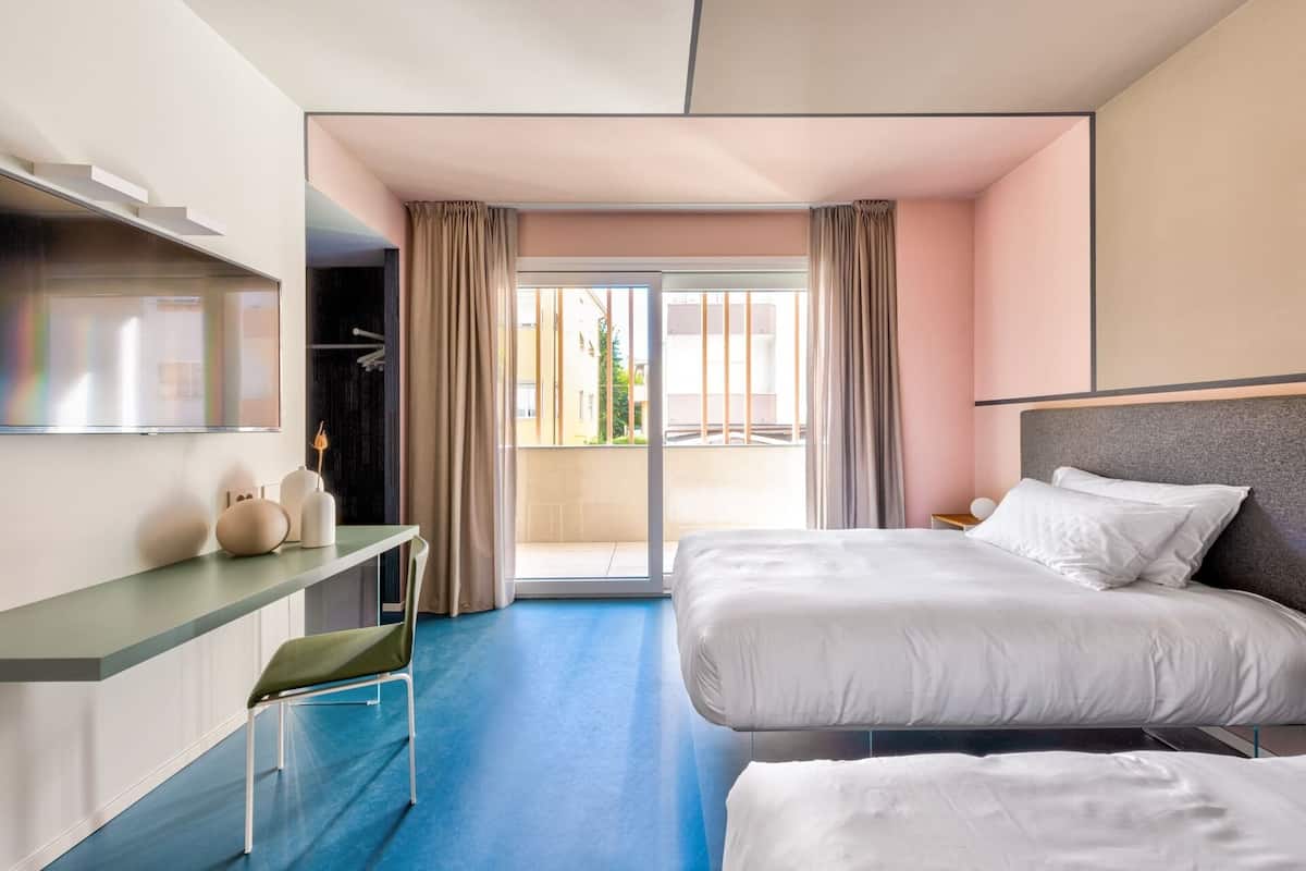 A hotel room with a bed, a desk, a chair, and a large window with curtains.