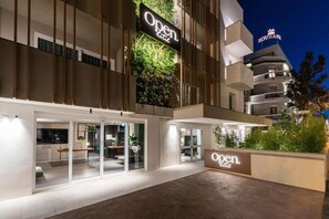 A modern hotel entrance with glass doors, a sign reading "Open Hotel", and a visible "SOVRAM" sign on the building. - Open Hotel (Rimini)