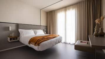 Ein modernes Hotelzimmer mit einem großen Bett, einem Nachttisch, einem Schreibtisch und einem Fenster mit Vorhängen.