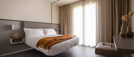 Una habitación de hotel moderna con una cama grande, una mesita de noche, un escritorio y una ventana con cortinas.