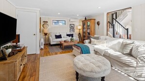 Un salon spacieux avec un canapé blanc, une table basse et un téléviseur posé sur un meuble en bois.