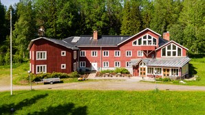 A large red wooden house with multiple windows and a balcony, surrounded by lush green trees. - Edsåsgården (Undersaker)