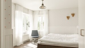A bedroom with a bed, a chair, and a window with curtains. - Edsåsgården (Undersaker)