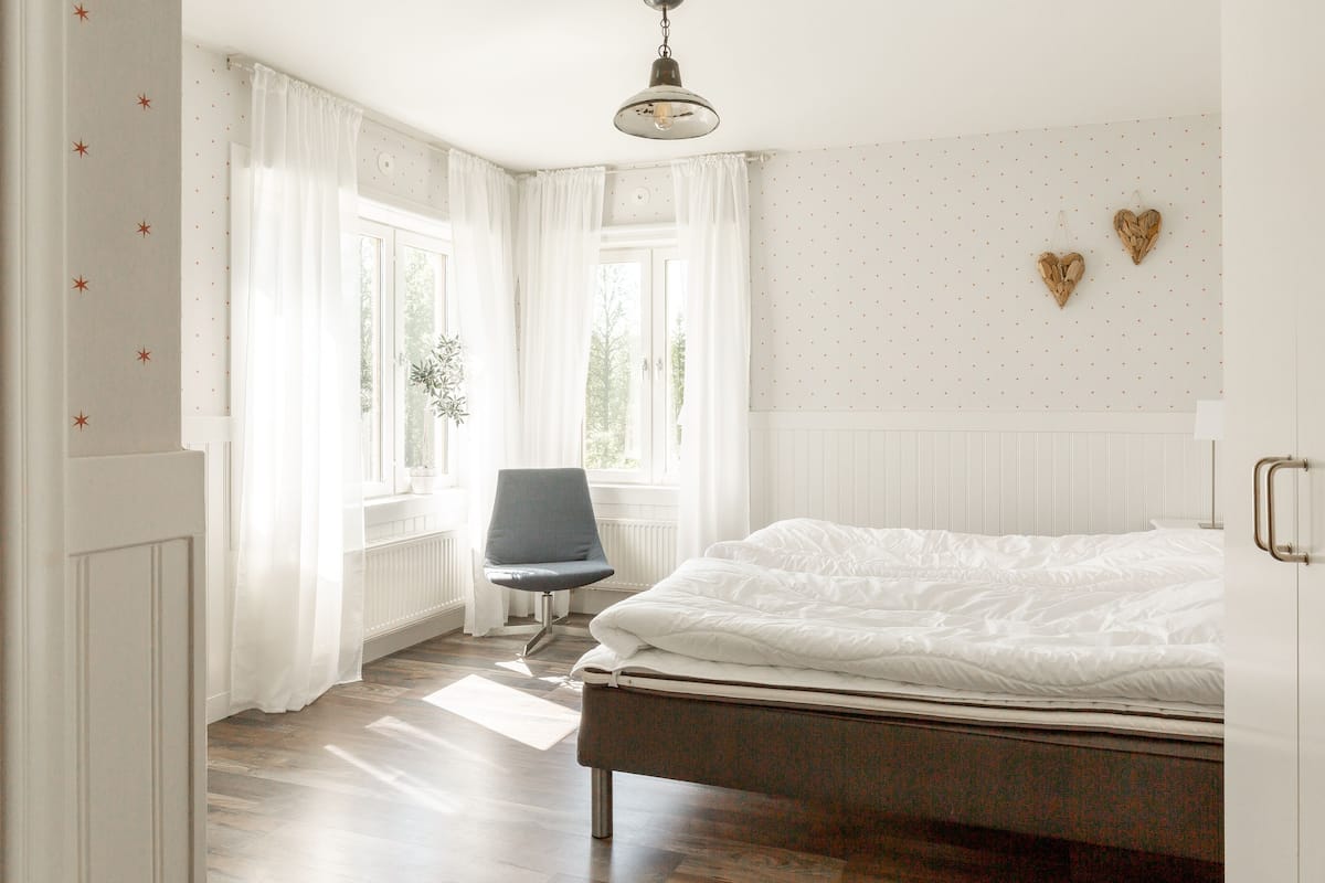 Un dormitorio con una cama, una silla y un ventanal con cortinas.