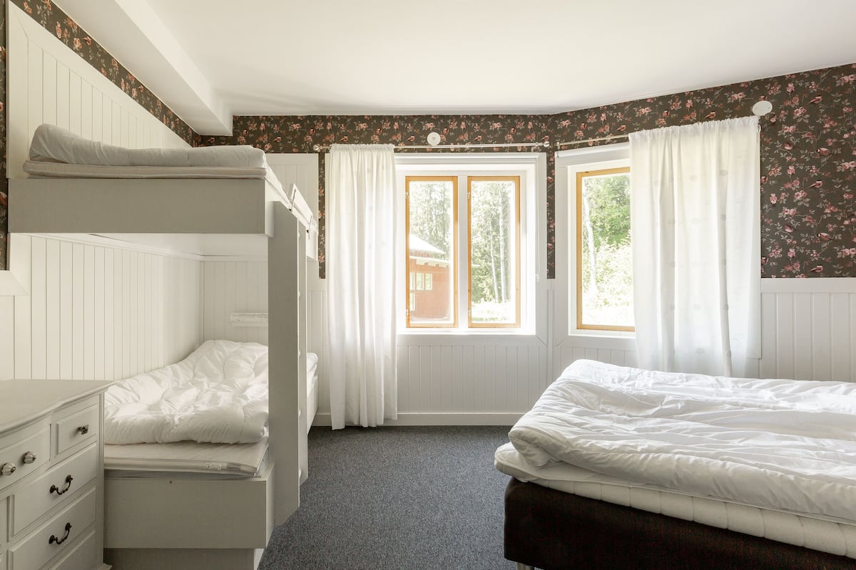 Un dormitorio con literas, un aparador y una ventana con cortinas.