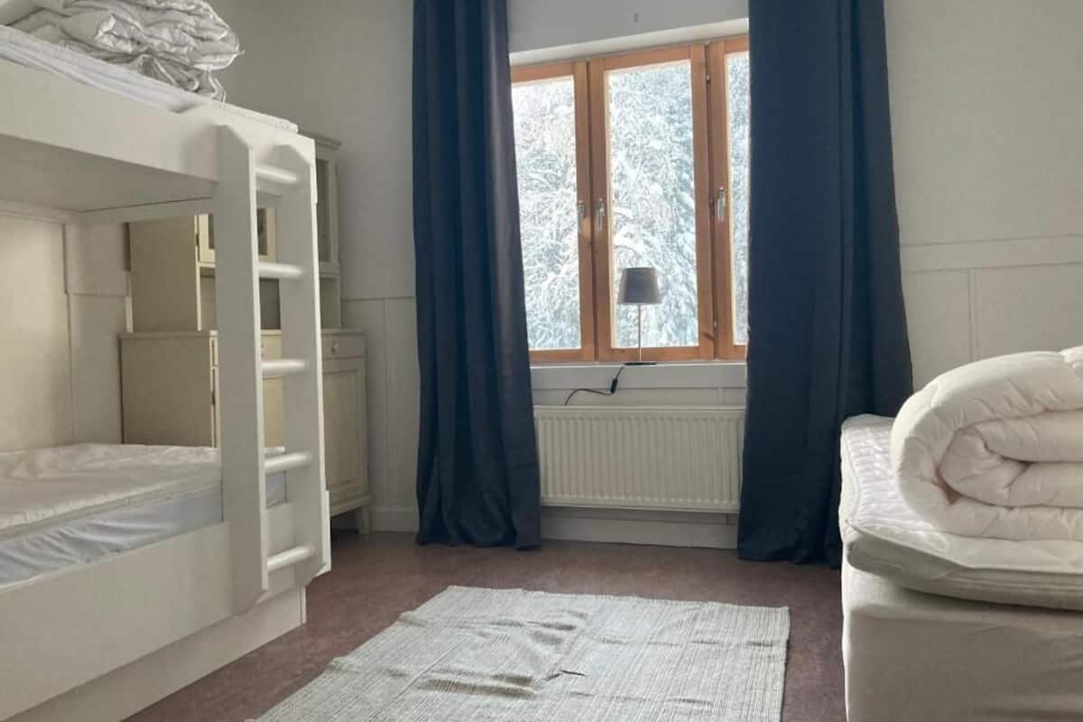 Un dormitorio con literas, una ventana con cortinas, un radiador y una mesita de noche.