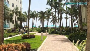 A pathway lined with palm trees and greenery, leading to a building with a modern design. - The Tides on the Beach by Aurich Designs (Hollywood)