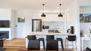 A modern kitchen with a central island, stainless steel appliances, and black bar stools.