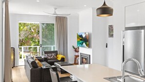 A modern living room with a sofa, a dining table, and a kitchen area with a refrigerator.