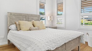 Un lit bien fait, recouvert d’une courtepointe blanche à texture intéressante, avec deux oreillers et une table de chevet sur laquelle se trouve une lampe.