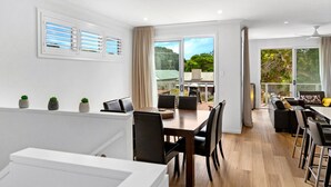 A modern, well-lit room with a dining area, a sofa, and a balcony with a view of greenery.