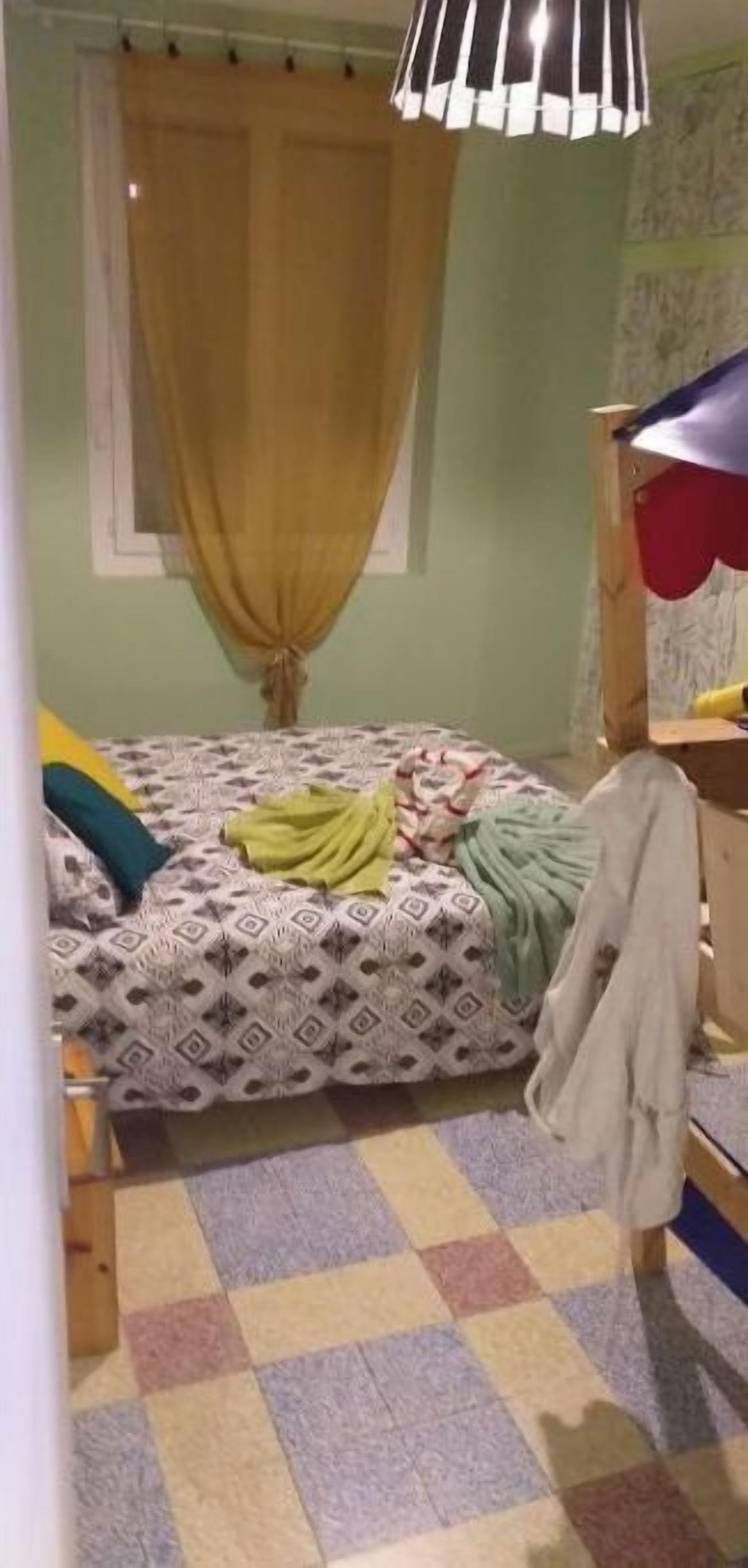 A bedroom with a bed, a window with curtains, a wooden bunk bed, and a checkered floor.