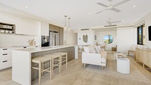 A modern kitchen with a central island, bar stools, and a dining area with a sofa and coffee table. - Escape 201 - Beachfront Luxury in Bilinga/ North Kirra - Linen Provided (Bilinga)